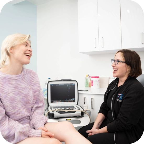 Double certified Dr Kamran Saraf Dr. Bonnie Mcklinley consults with a patient in a clinical setting, using a tablet to review medical information. An ultrasound machine is positioned in the background, highlighting the focus on diagnostic venous care.