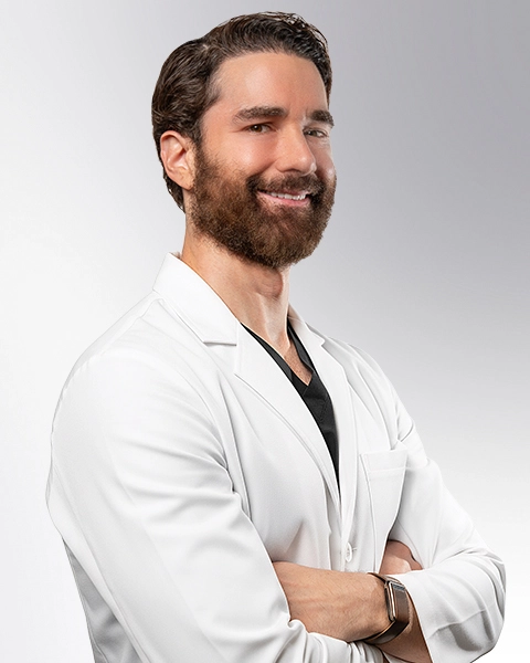 Dr. Shaun Cole, board-certified vein doctor at Vein Treatment Clinic, smiling in a white coat with arms crossed.